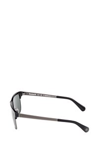 Černé sluneční brýle Timberland s šedými spánky, tmavě zabarvenými skly a logem na spánkových ramenou a na koncích spánků.