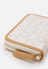 Beige Lederbrieftasche mit texturiertem Finish, ausgestattet mit einem goldfarbenen Reißverschluss, Logo-Muster und sandfarbenen Akzenten. Kompakte rechteckige Form.