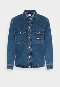 Giacca di denim di colore blu scuro con maniche lunghe, chiusura a bottoni a scatto, due tasche sul petto e una toppa con logo sulla tasca sinistra.