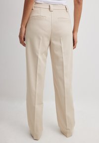 Beige tailored trousers with a textured fabric; wide-leg cut, front pleats, and two back pockets. Clean, minimal design.