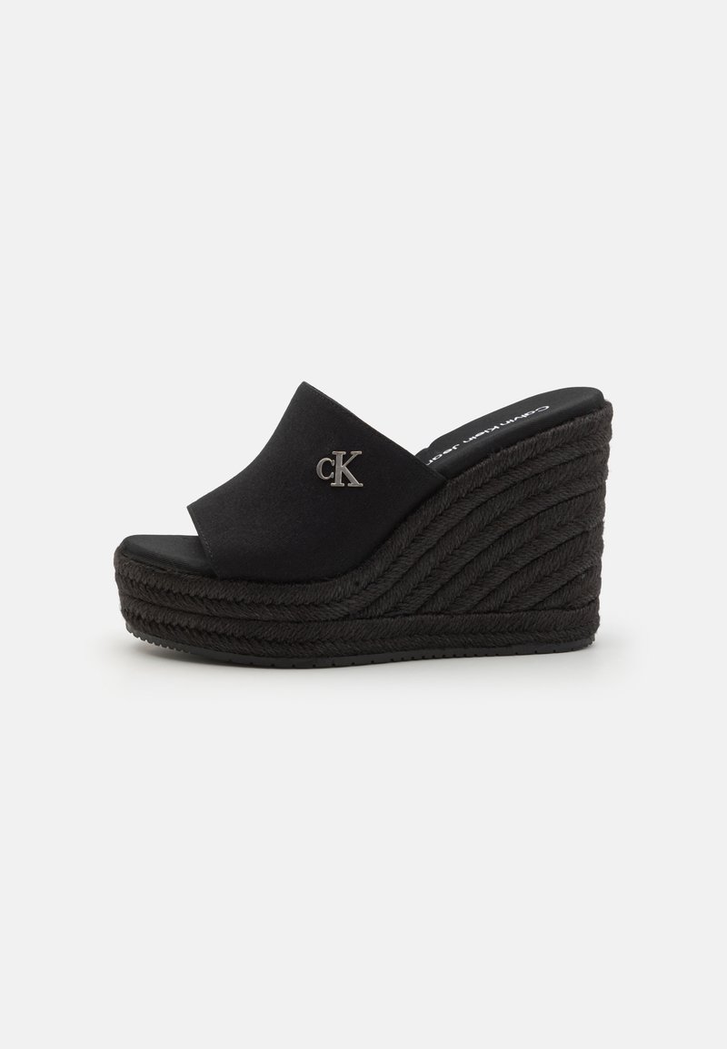 Sandalias cuñas negras con una suela gruesa y texturizada. La parte superior de tela suave cuenta con un acento de logo en piel de becerro. Estilo fácil de poner con un diseño de punta abierta.