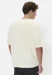 Krémový pletený shirt s krátkými rukávy, kulatým výstřihem a mírně uvolněným střihem; texturovaná látka s hladkým povrchem.
