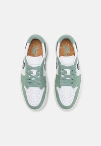 Paire de baskets Nike blanches et vertes avec des bouts perforés, des logos swoosh noirs et des semelles intérieures à texture de liège vues de dessus.