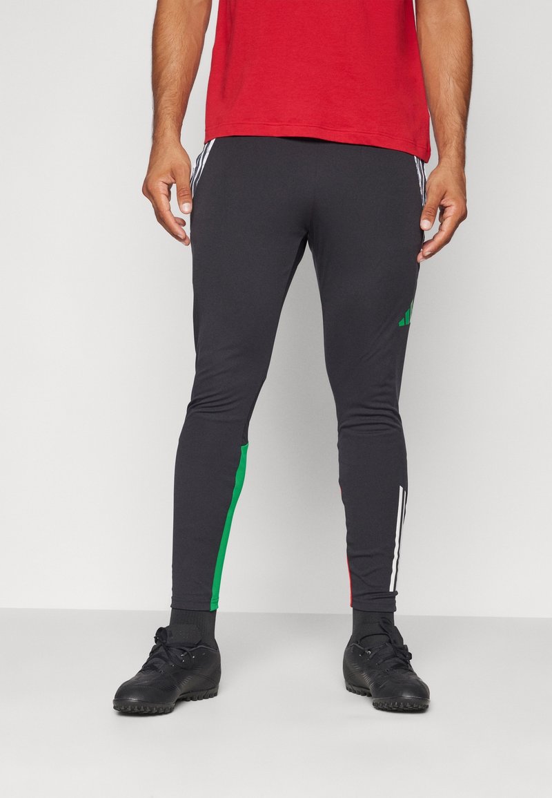 Un pantalon de sport noir doté de bandes latérales vertes et rouges, avec des accents blancs. Il est ajusté et fabriqué en matière extensible, idéal pour le sport.