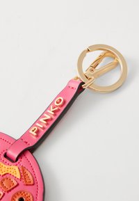 Gullnøkkelring med et rosa lærreim preget med "PINKO" festet til et rosa og oransje sydd design.