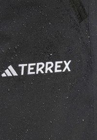 Črn vodoodporen material z vidnimi kapljicami in belim logotipom "TERREX." Teksturna površina nakazuje odpornost proti vlagi.