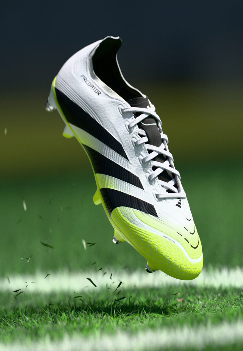 Pantofila de fotbal albă și neagră, cu o suprafață texturată și accente vibrante de galben, având un design cu șireturi și o formă ușoară, aerodinamică.