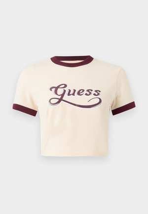 T-shirt crema cropped con colletto e polsini a coste color bordeaux, con un audace logo "Guess" in corsivo di colore rosso scuro.