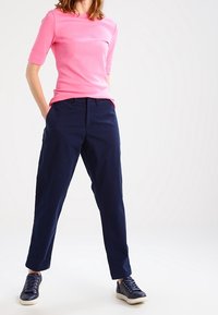 Ljusrosa kortärmad topp tillsammans med marinblå avslappnade byxor och mörkblå sneakers. Toppen har en rundad halsringning och en figurnära design.