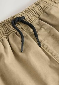 Pantalones cortos color caqui con cintura elástica y cordón negro. El material es suave con una textura lisa; el diseño incluye detalles de costura visibles.