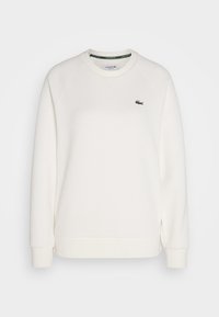 Sweat-shirt blanc à manches longues avec col rond, poignets et ourlet côtelés, arborant un petit logo crocodile Lacoste vert foncé sur le côté gauche de la poitrine.