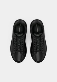 Baskets en cuir noir avec fermeture à lacets, bout rond, col rembourré et accents de logo discrets. Texture lisse et design élégant.