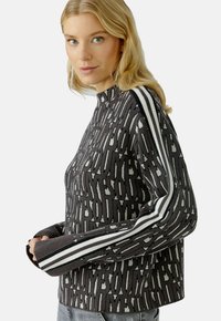 Zwart gebreid sweater met een gestructureerd patroon, voorzien van witte strepen op de mouwen en een hoge hals. Accenten van grijs overal.