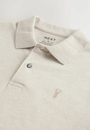 Maglietta polo beige con colletto, patta a due bottoni e un piccolo logo ricamato. Tessuto morbido con una finitura testurizzata. Vestibilità regolare.