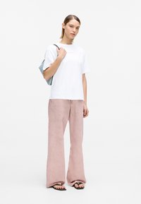 Valge lühikeste varrukatega T-särk roosade tähtedega, kombineeritud heledate roosade laia lõikega pükstega ja mustade varbavaheplätudega. Model kannab sinist kotti.