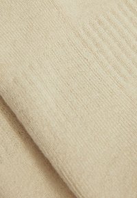 Beige strikket stof med en glat tekstur, der har subtile diagonale ribbede mønstre og ensartet, fin søm hele vejen igennem.