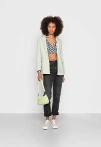 Blazer verde claro, jeans pretos de cintura alta, top cropped em padrão xadrez, bolsa verde e ténis claros; tecidos texturizados e corte descontraído.