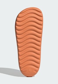 Suola di scarpa in gomma arancione con una texture ondulata e un accento circolare nella parte inferiore. Progettata per trazione e flessibilità.