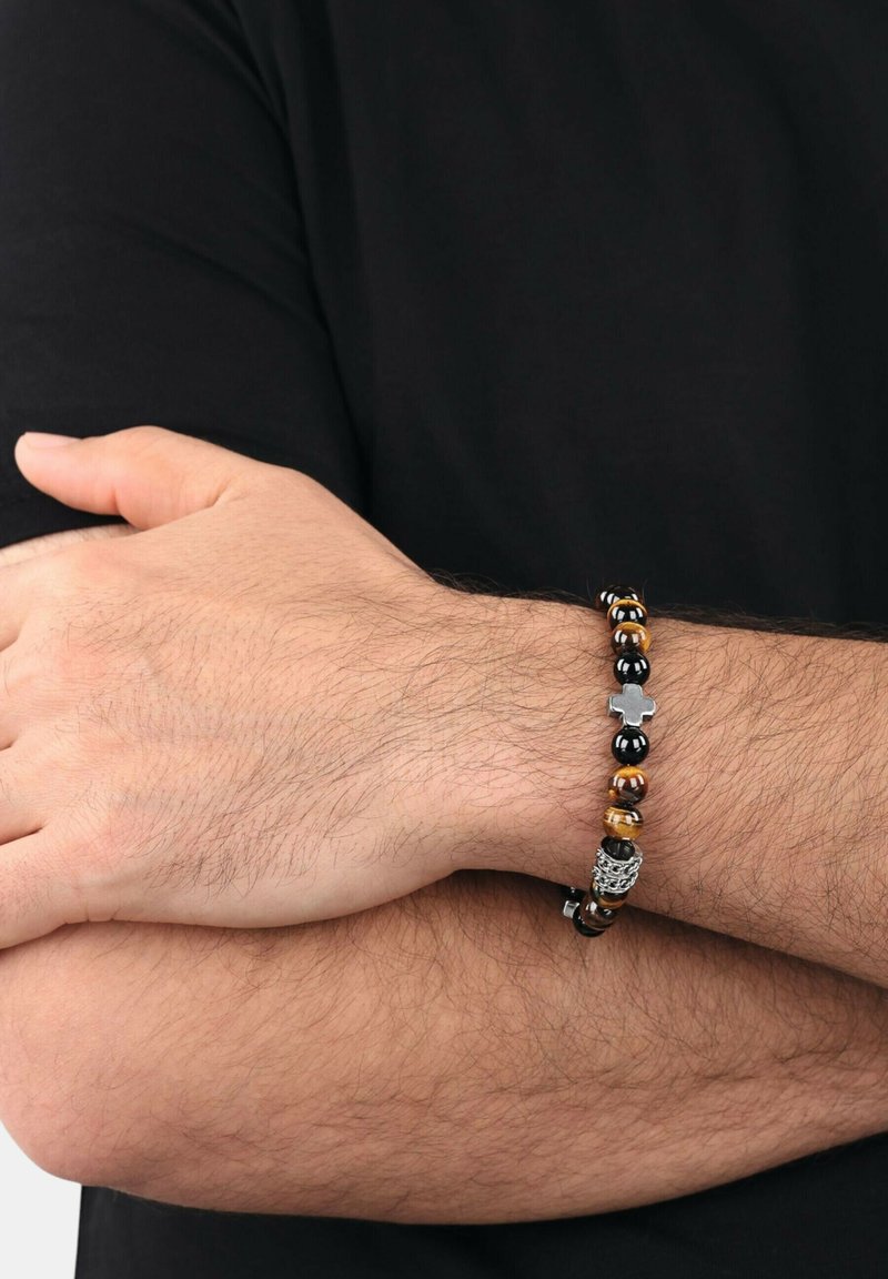 Pulsera de cuentas con ojo de tigre marrón, cuentas negras y un acento de cruz en tono plateado; diseño flexible con textura suave.