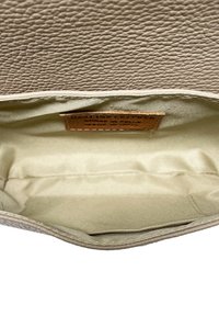 Interno di una borsa in pelle beige con superficie texturizzata, foderato liscio e un'etichetta in pelle che indica l'autenticità, caratterizzata da un design semplice.