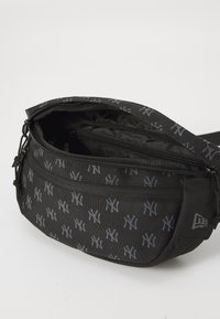 Sac bandoulière noir avec un motif en gris répétitif, en matériau texturé, comportant des compartiments à fermeture éclair et une sangle ajustable.
