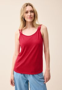 Top sin mangas rojo con detalles de tirantes fruncidos, textura suave, tela ligera y escote redondeado, combinado con pantalones azul claro.