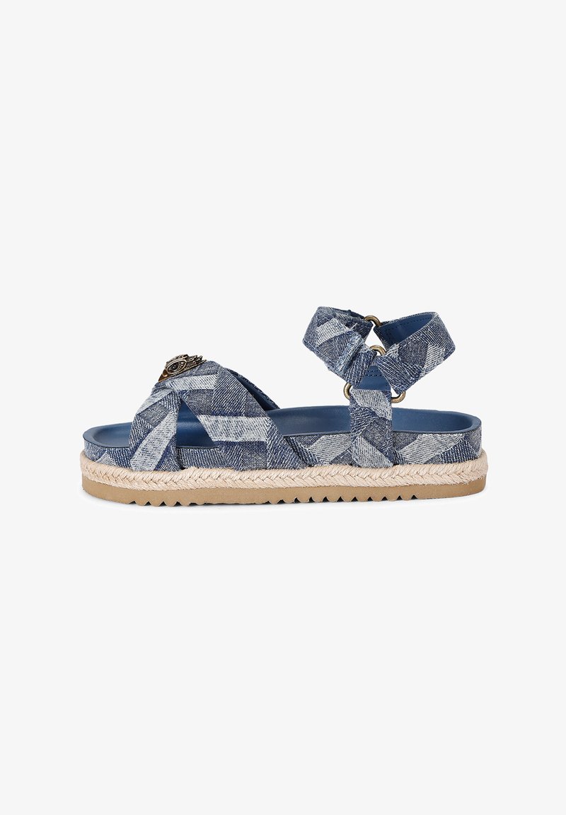 Sandale espadrille en denim bleu avec des brides croisées, enroulement autour de la cheville et semelle en jute tissé. Présente un accent décoratif en matériel à l'avant.