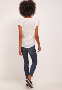 Bílé tričko s krátkým rukávem a krajkovými detaily na ramenou, spárované s tmavě modrými skinny džíny a černými teniskami.