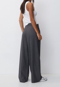 Pantalons à jambe large en maille gris avec une taille lisse et deux poches arrière. Associés à un débardeur blanc et des baskets décontractées.