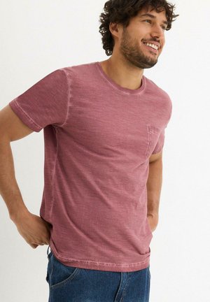 T-shirt a maniche corte, con scollatura a girocollo, di colore rosa tenue. Realizzato in un tessuto morbido e testurizzato, con taschino sul petto e una vestibilità leggermente rilassata.