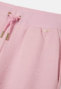 Pantacourt rose clair en tissu texturé, avec un motif de logo en relief, un cordon de serrage avec des éléments en or, et un discret accent logo.