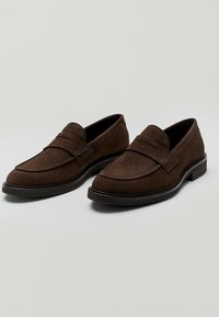 Brune ruskinds loafers med en glat overflade, rund tå og dekorativ remdetalje. Har en solid sort ydersål for stabilitet.