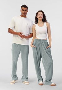 Deux modèles se tiennent ensemble. L'homme porte un t-shirt blanc à manches courtes et un pantalon rayé gris. La femme porte un crop top blanc et un pantalon large bleu clair avec des poches.
