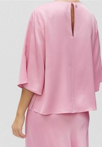 Top di seta rosa con maniche a tre quarti, caratterizzato da una chiusura a oblò sul retro. Texture liscia e vestibilità ampia, che offre una silhouette rilassata.