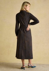 Brūns midi kleita ar tumši ziliem leoparda traipiem, garām piedurknēm un jostu. Valkāta ar zilām slingback papēžiem ar norādītu purngalu.