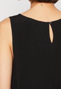 Top noir sans manches avec un col rond et une fermeture à bouton en fente à l'arrière. Tissu doux avec une texture lisse.