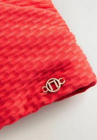 Tessuto rosso con una trama strutturata. Presenta un accento di metallo dorato circolare sul bordo, che arricchisce il dettaglio del design.
