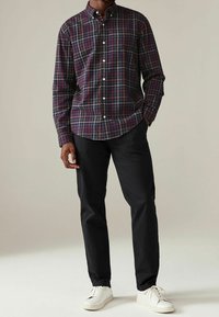 Camicia con bottoni e motivo a quadri multicolore in blu navy scuro, bordeaux e giallo. Indossata con pantaloni neri e scarpe da ginnastica bianche.