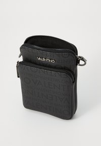 Sac noir avec fermeture éclair en tissu texturé, arborant un nom de marque en relief. Design compact avec deux compartiments pour organiser. Accents en matériel argenté.