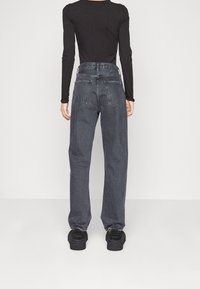 Jeans grigi a vita alta, a vestibilità ampia, con gamba dritta, cuciture minime e due tasche posteriori, abbinati a calzature nere.