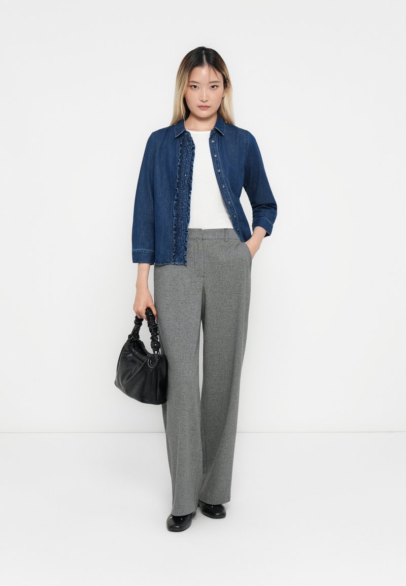 Chemise en denim avec détail volanté, haut blanc, pantalon large à carreaux gris, sac à main noir et chaussures fermées noires.