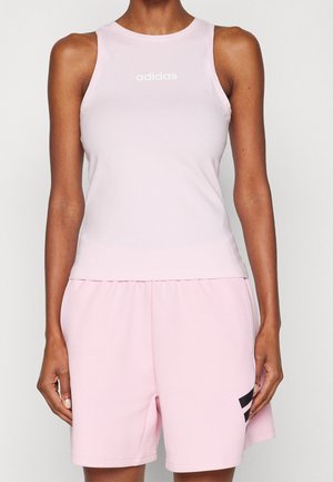 Woman wearing light pink sleeveless Adidas top and matching shorts with black logo on right leg against plain background.