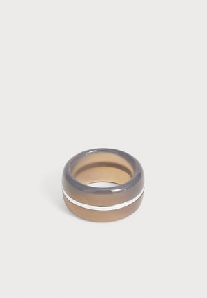 Bague large lisse avec une bande translucide ambre et grise, avec une fine bande argentée horizontale au milieu sur un fond clair.