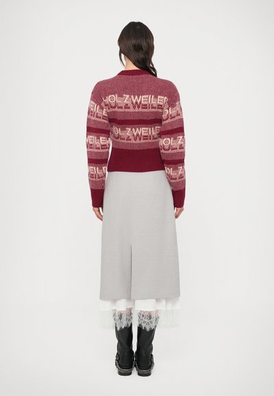 Pleteni pulover z bordo in kremasto barvnimi vodoravnimi črtami, z večkratnim napisom. Kombiniran z sivo krilom in črnimi škornji do kolen.