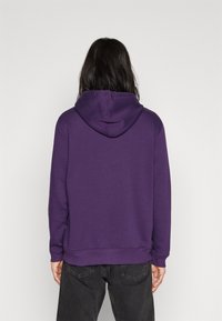 Sudadera morada con bolsillo canguro y capucha ajustable, hecha de una tela suave con puños y dobladillo acanalados, vista desde la parte de atrás.
