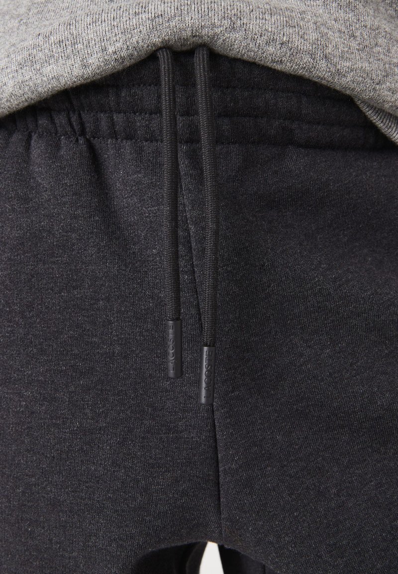 Primo piano dell'elastico dei pantaloni della tuta grigio scuro con lacci e una vista parziale di una maglia grigio chiaro sopra.