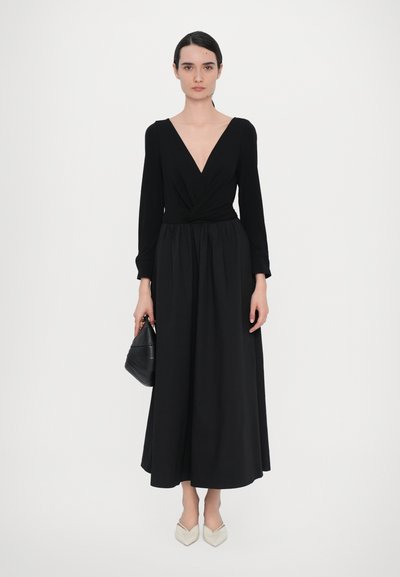 Juoda ilgomis rankovėmis su V formos iškirpte ir susuktos liemens suknelė, laisvai krentantis sijonas, derinamas su juoda rankine ir kremine aštriais bateliais.