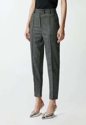 Pantaloni grigi su misura in tessuto texturizzato con vita alta, chiusura con bottone e fessure laterali per un dettaglio aggiuntivo. Abbinati a tacchi alti metallici.
