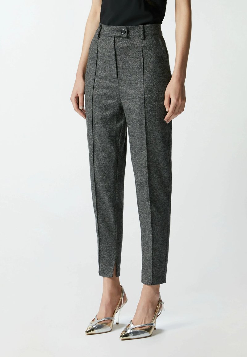 Pantaloni grigi su misura in tessuto texturizzato con vita alta, chiusura con bottone e fessure laterali per un dettaglio aggiuntivo. Abbinati a tacchi alti metallici.