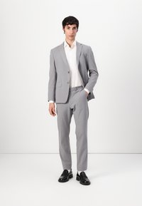 Light gray suit with a notch lapel, two-button closure, slim-fit trousers, and a white shirt; worn with black loafers. Solid color, smooth texture.